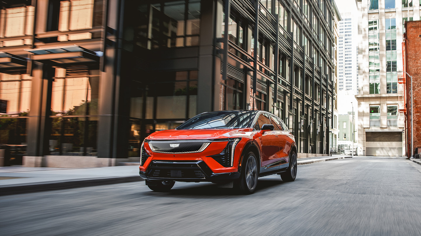 A sleek orange SUV drives through a city street surrounded by tall buildings.