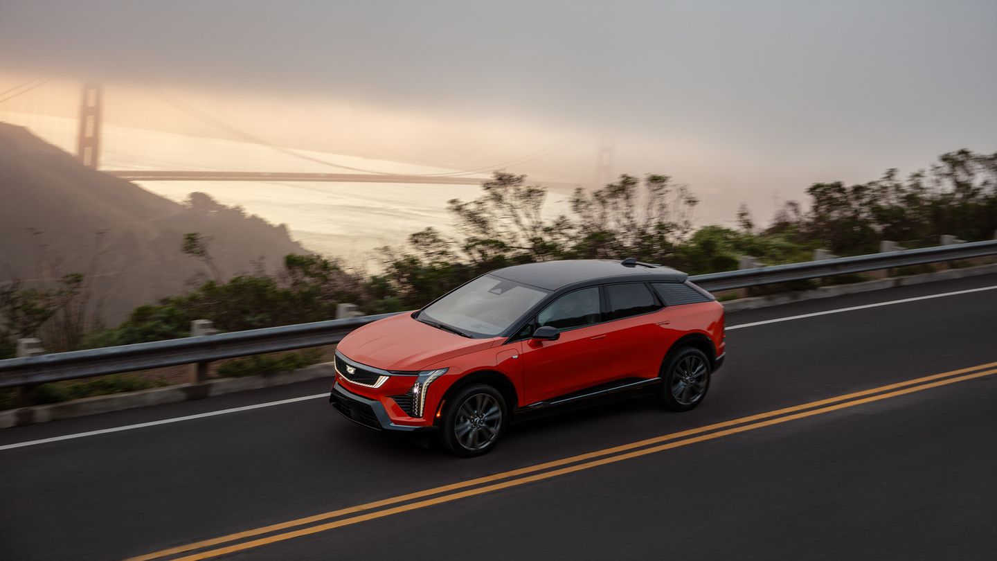 Red SUV driving on a coastal road with the Golden Gate Bridge visible in the background.