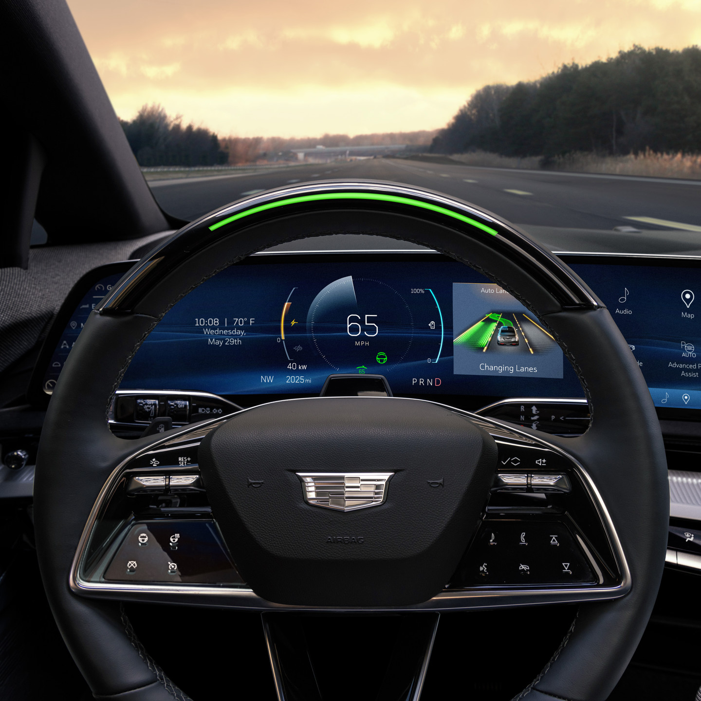 View from inside a car showing a cyclist crossing the street at an intersection in a city. The dashboard displays controls and information. Sunlight and shadows create a clear, bright scene.