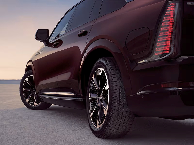 Rear view of a maroon SUV with sleek design and illuminated taillights at dusk on an open road.