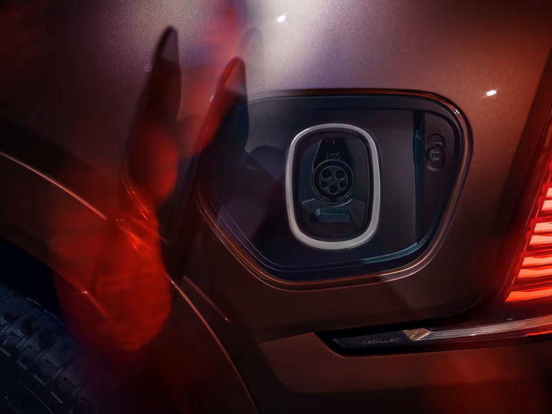 Electric vehicle charging port on a Cadillac, accentuated by red lighting.